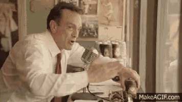 a man is talking into a microphone while sitting at a desk .