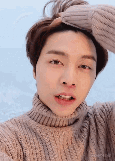 a close up of a person wearing a turtleneck sweater with their hand on their head