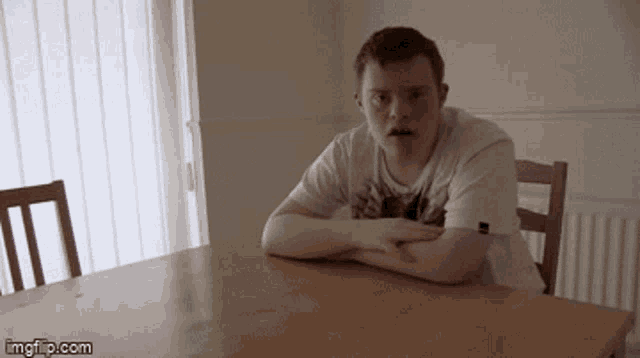 a man with down syndrome is sitting at a table with his arms crossed and looking at the camera .