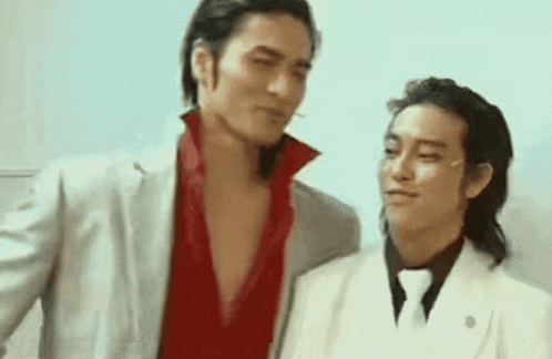 two men are standing next to each other and one is wearing a red shirt and a white suit .