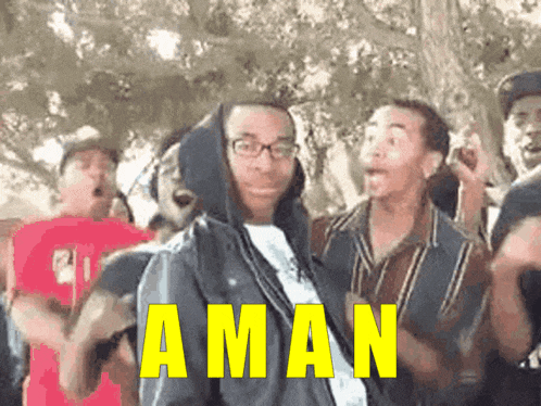a man in a hooded jacket stands in front of a group of people with the word aman written in yellow
