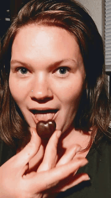 a woman with a nose ring is holding a chocolate heart in her mouth