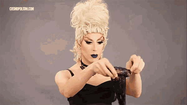 a drag queen wearing a wig and a black dress is holding a black lace glove .
