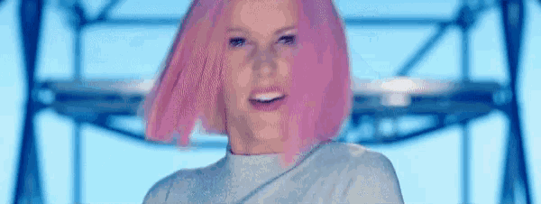 a woman with pink hair and a white shirt is smiling .