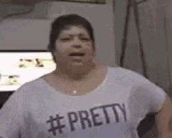 a woman wearing a white shirt with the word pretty on it is standing in front of a television .