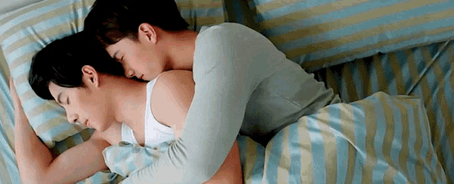 two men are sleeping on a bed with striped sheets .