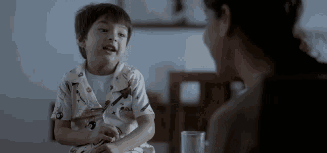 a little boy is sitting at a table with a woman talking to him .
