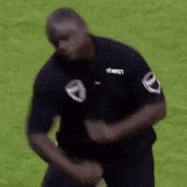 a man in a black shirt is standing on a soccer field with his hands on his hips .