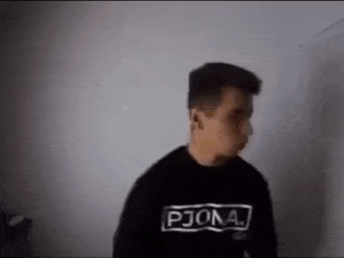 a man wearing a black sweater is standing in front of a wall .
