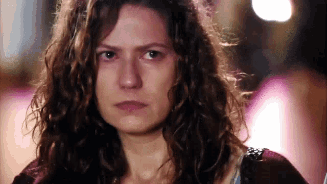 a woman with curly hair is looking at the camera with a serious look on her face