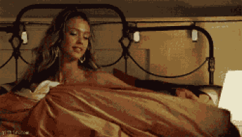 a woman is laying on a bed with a man sleeping in the background