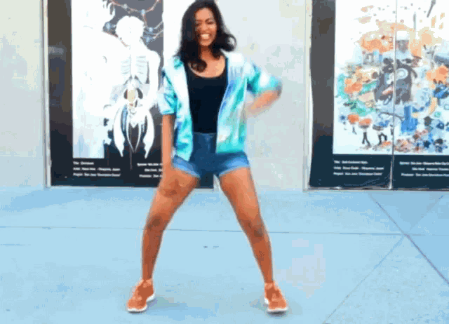 a woman in shorts is dancing in front of a wall with paintings on it