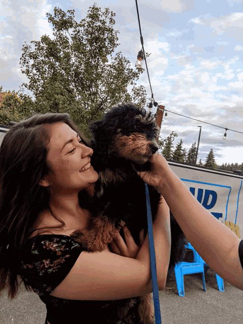 a woman holds a small black dog in front of a sign that says ud