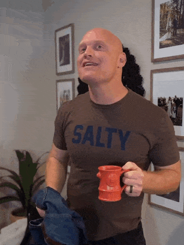 a man wearing a salty t-shirt holds a red mug