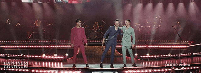 three men on a stage with the words happiness continues on the bottom right