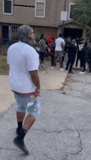 a man in a white shirt and shorts is walking down the street in front of a crowd of people .