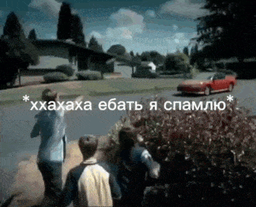 a red car is driving down a street with a group of people standing on the side of the road