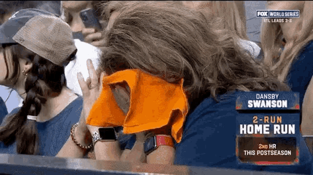 a woman covering her face with an orange towel while watching a baseball game