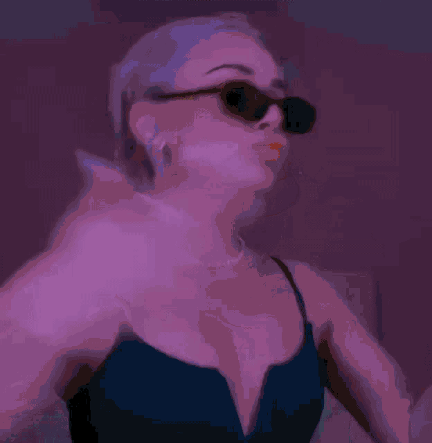 a woman wearing sunglasses and a green tank top is blowing a kiss