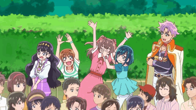 a group of people are standing in front of a green hedge with their hands in the air