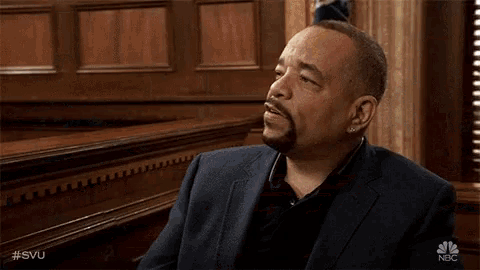 a man in a suit is sitting in a courtroom talking to another man .