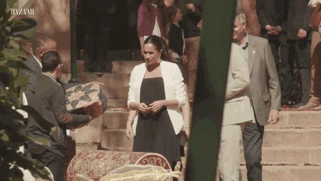 a woman in a black dress is standing in front of a group of people with the word bazaar on the bottom right corner