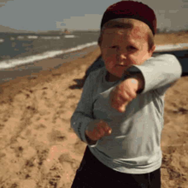 a young boy wearing a red hat is standing on a beach