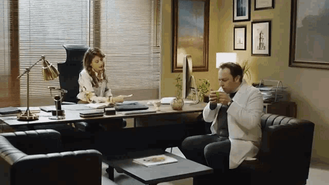 a man in a lab coat is drinking from a cup while sitting in front of a woman in a chair