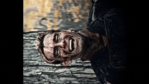 a man with blood on his face is laying on his back on a wooden surface .