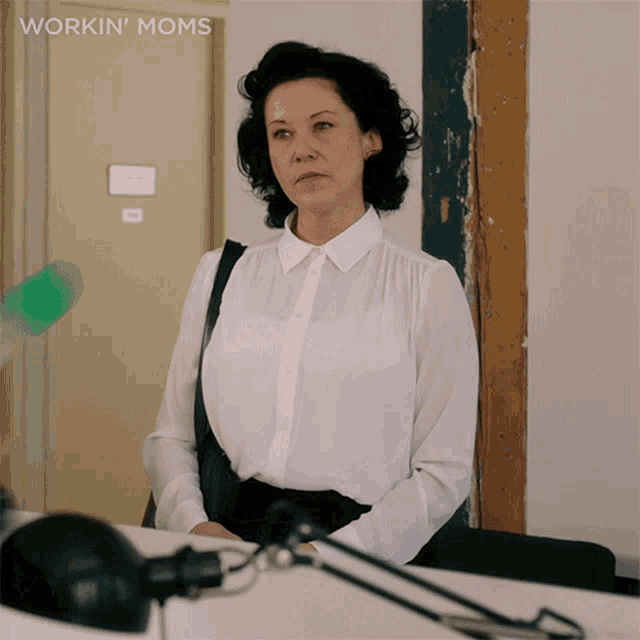 a woman in a white shirt is standing in front of a door with the words workin ' moms above her
