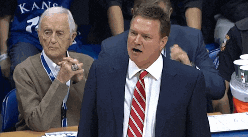 a man in a suit and tie stands in front of an older man in a kansas jersey