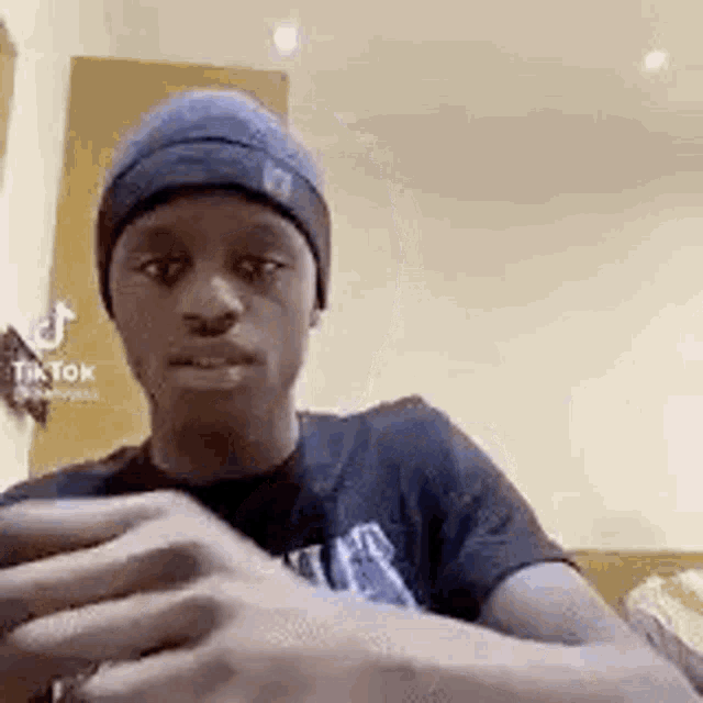 a young man wearing a beanie and a t-shirt is sitting in a living room .