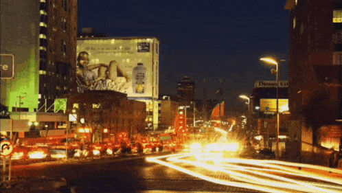 a busy city street at night with a billboard for a bottle of ice tea