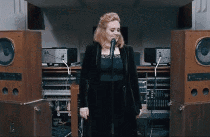 a woman in a black jacket is singing into a microphone in front of a row of speakers .