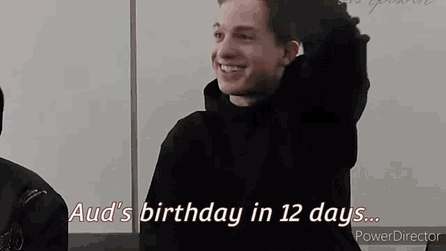 a young man in a black hoodie is smiling and holding his hair in front of a white board .