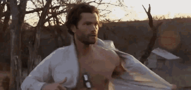 a shirtless man in a white shirt is standing in a field with his shirt off .
