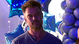 a man is standing in front of a bunch of blue balloons and looking at the camera .