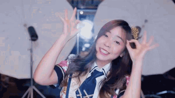 a girl in a school uniform is making an ok sign with her hands in the air .