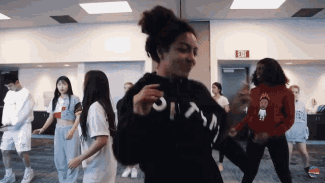 a group of people are dancing in a room with a red exit sign
