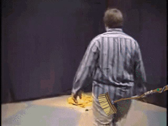 a man in a striped shirt is holding a broom in his back