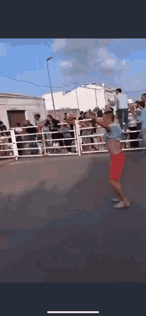 a man in red shorts is dancing in front of a crowd of people behind a fence .