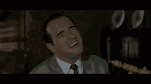 a man in a suit and tie is laughing while holding a gold necklace .