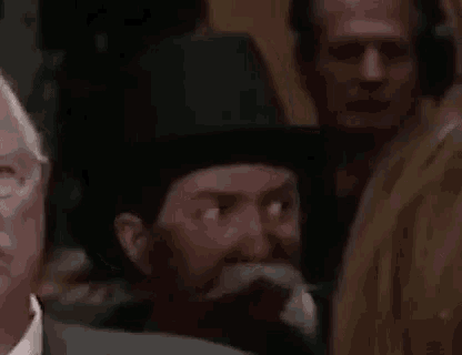 a man with a mustache and a hat is sitting in a crowd .