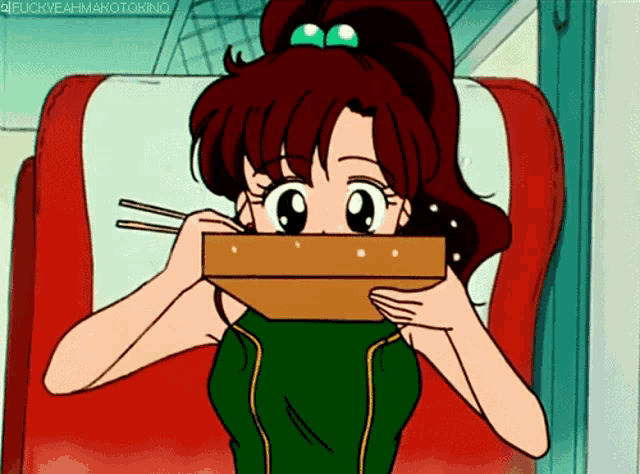 a girl in a green shirt is holding a box with chopsticks in front of her mouth
