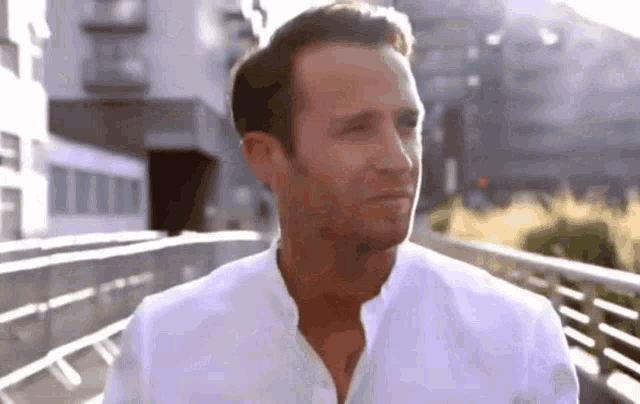 a man in a white shirt is standing on a bridge looking at the camera .