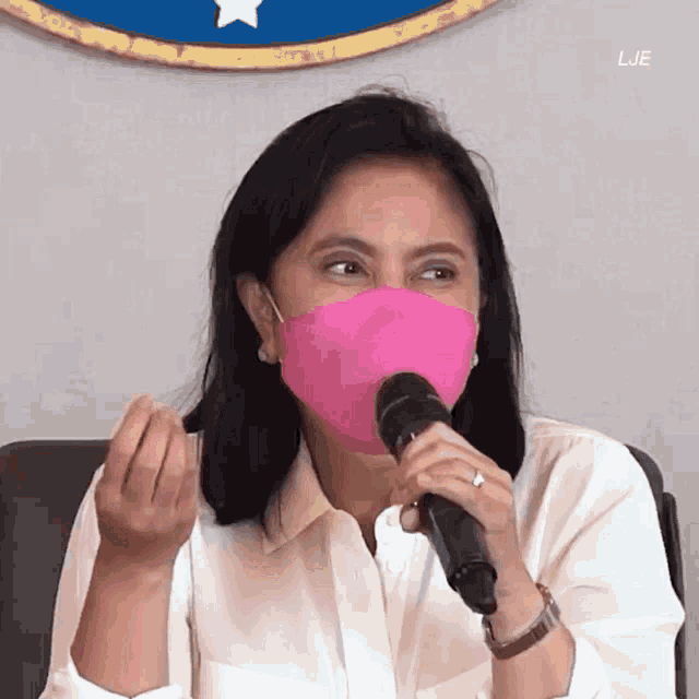 a woman wearing a pink mask holds a microphone