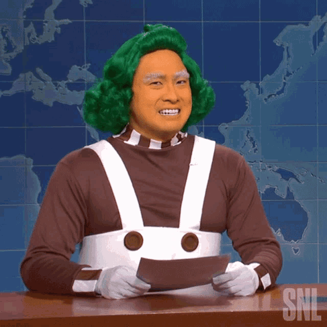 a man in a green wig holds a piece of paper in front of a snl sign