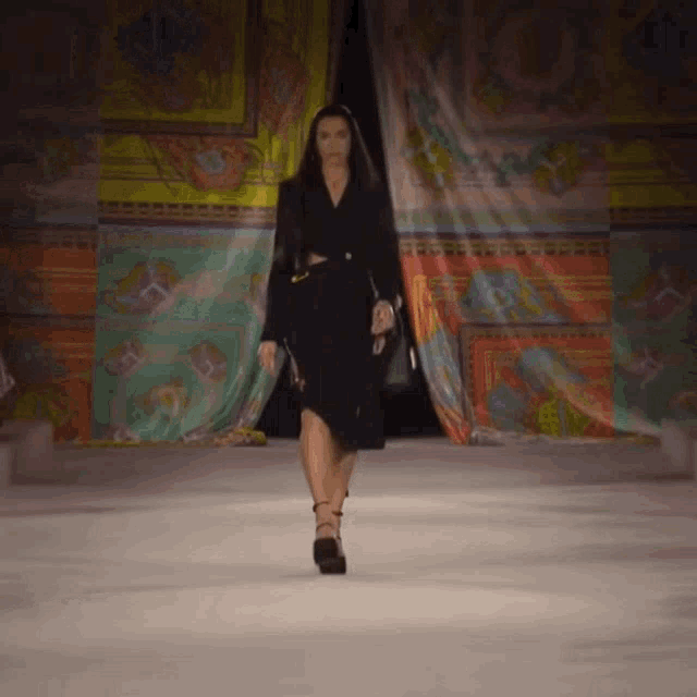 a woman is walking down a runway at a fashion show wearing a black dress and a black jacket .