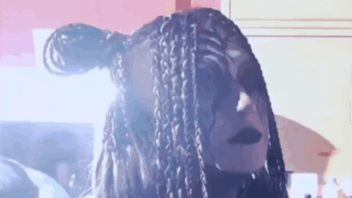 a woman with dreadlocks and black makeup is standing in front of a pink wall .