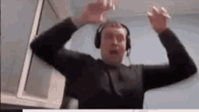 a man wearing headphones is standing in front of a computer screen with his arms in the air .